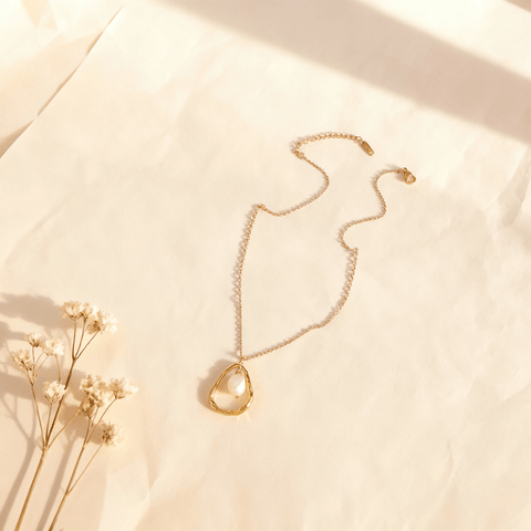 A macro shot of the single freshwater pearl from The Luna Pearl necklace, positioned to catch soft, natural light. The image captures the subtle, iridescent orient and the soft, moon-like glow of the pearl's surface.