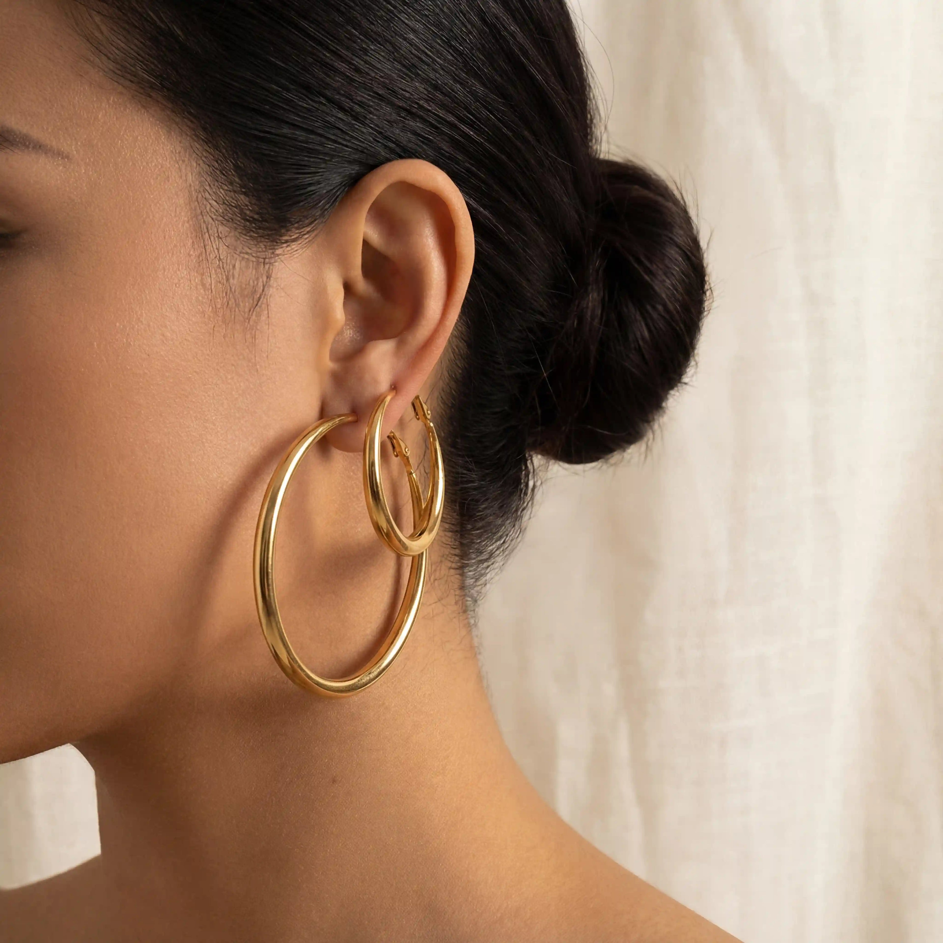 Close up of model wearing stacked Mneme gold hoop earrings in large and medium sizes.