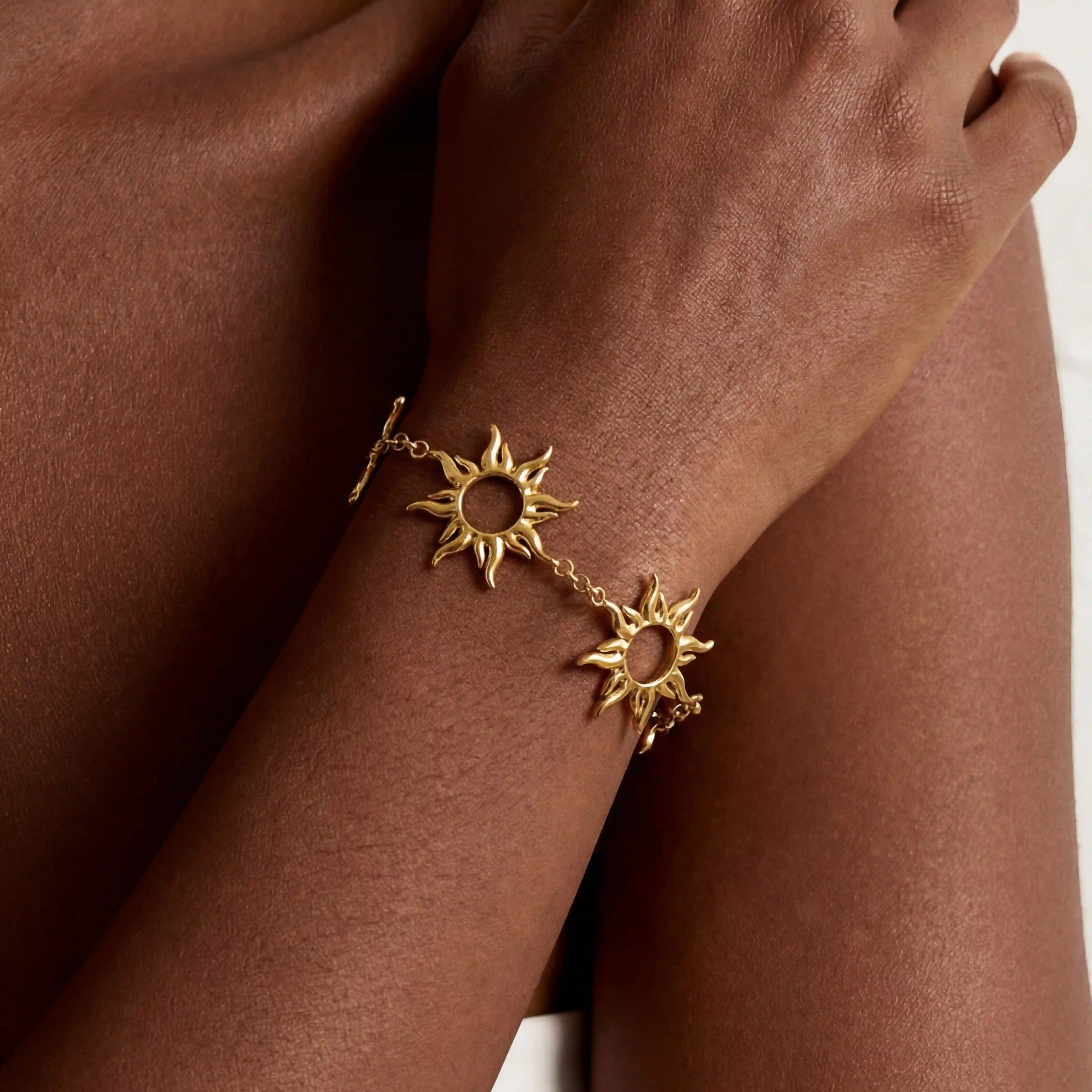Close up of dark skin model wearing gold radiant sun charm bracelet celestial jewelry.