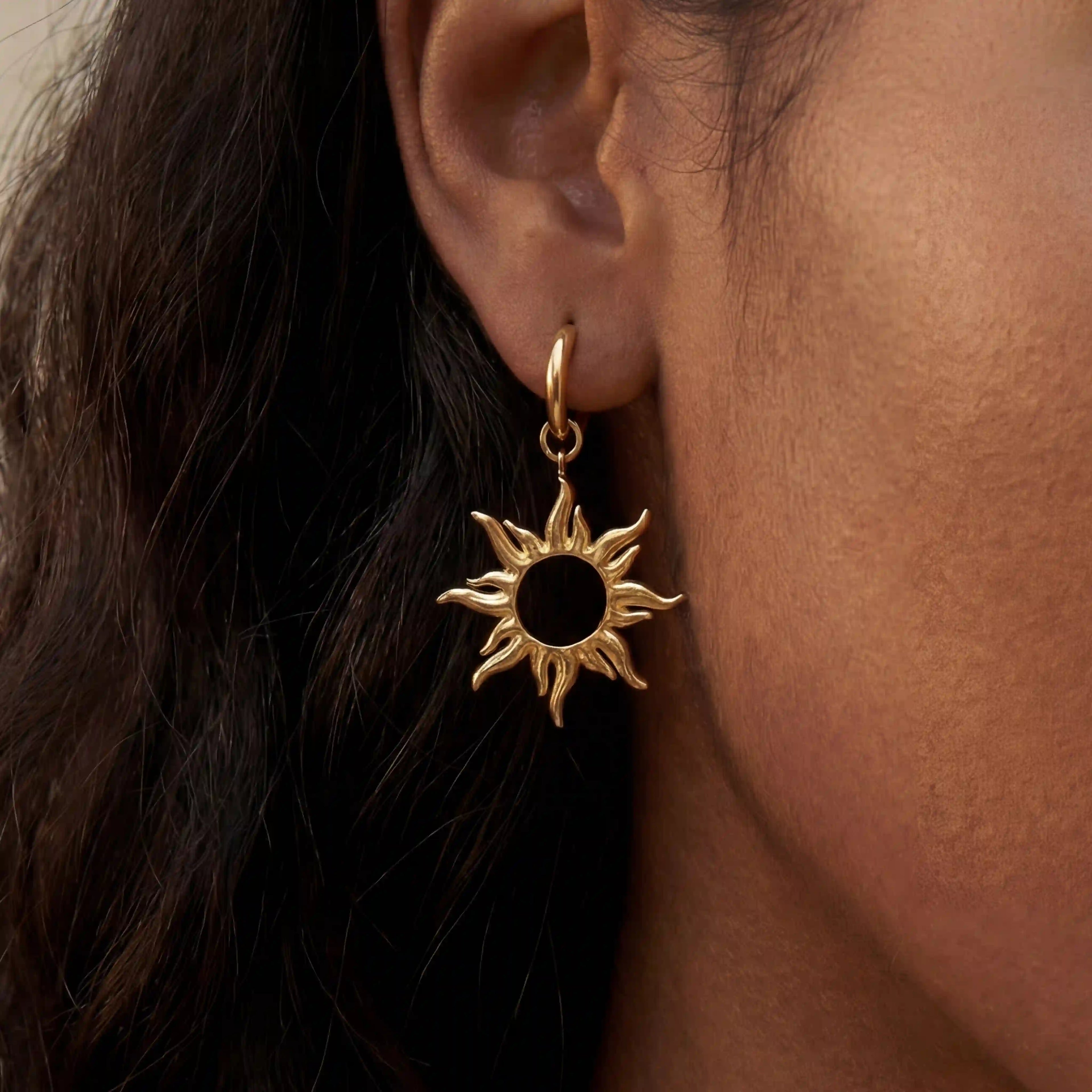Close up of woman with dark skin wearing gold radiant sun charm drop earrings celestial jewelry.