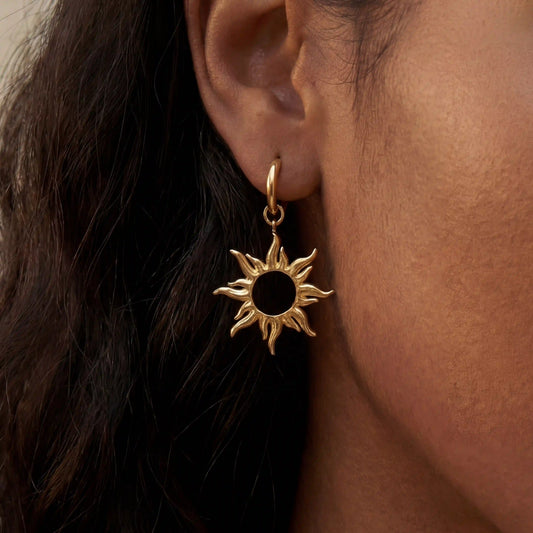 Close up of woman with dark skin wearing gold radiant sun charm drop earrings celestial jewelry.