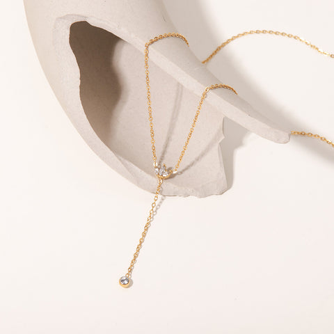 An artistic flat lay of The Reine Necklace on a white silk background with dramatic shadows, emphasizing its delicate sparkle and sophisticated Y-shape.