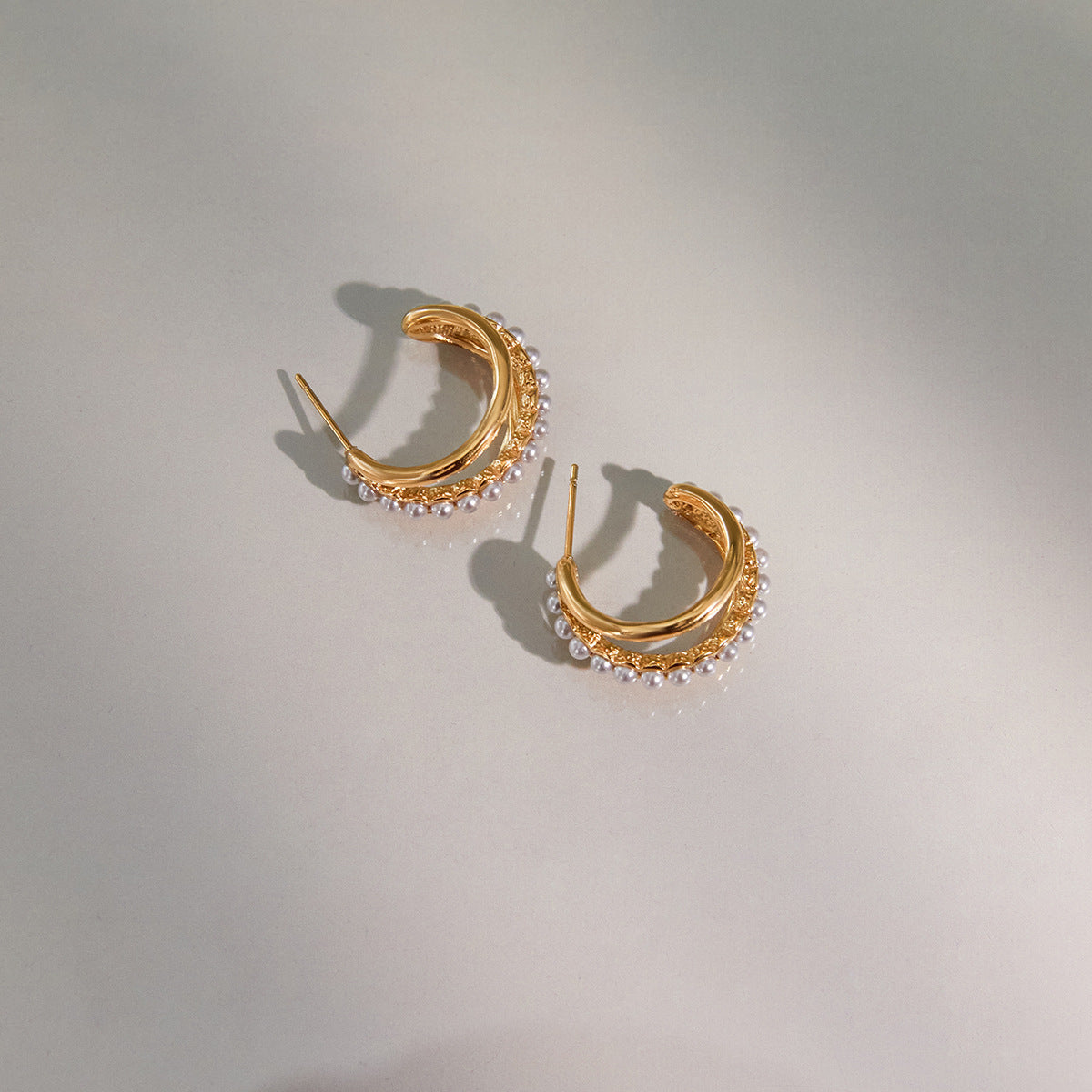 An artistic shot of The Siren Hoops in dramatic lighting, casting a soft shadow to emphasize their sculptural, three-dimensional form.