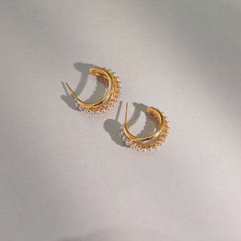 An artistic shot of The Siren Hoops in dramatic lighting, casting a soft shadow to emphasize their sculptural, three-dimensional form.