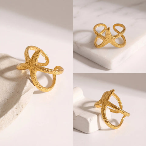 Aesthetic flat lay of sand textured gold starfish ring details on white stone.