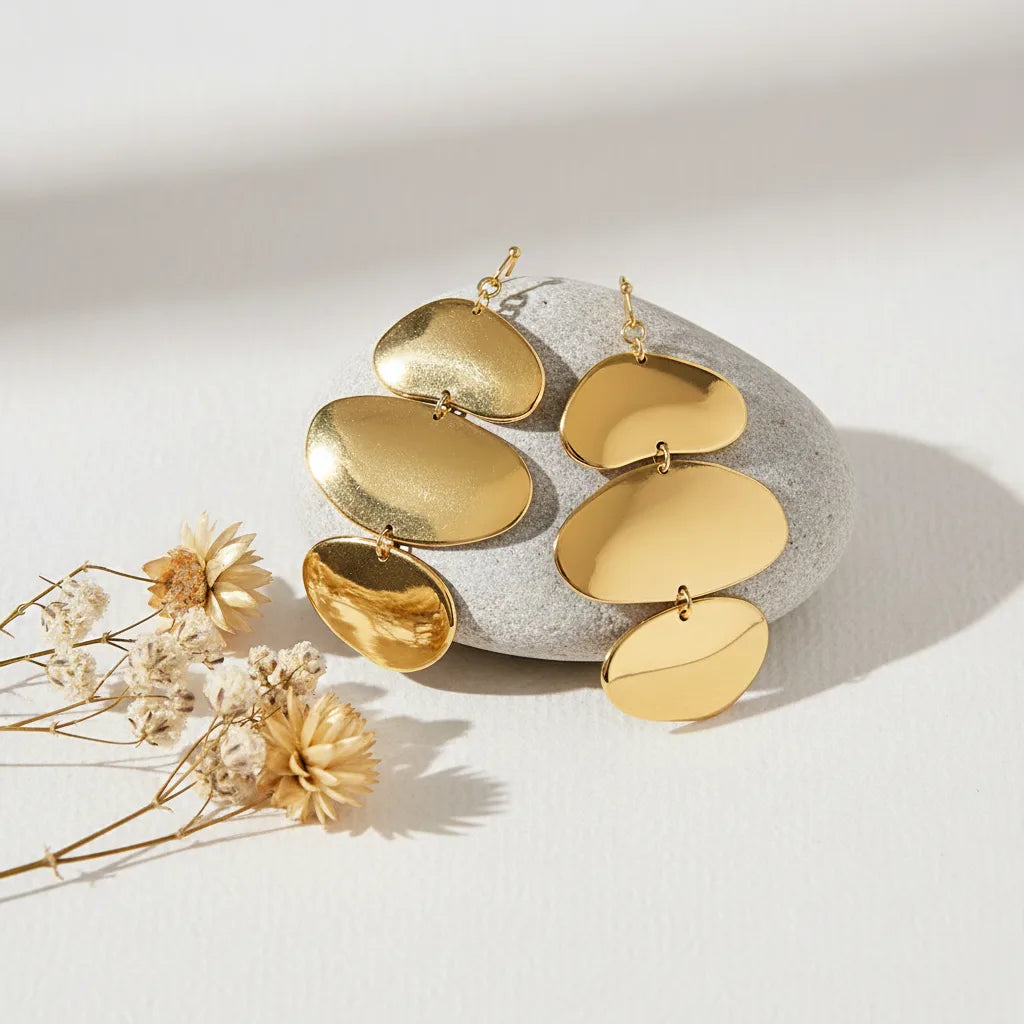 An artistic flat lay of The Thalia Earrings on a display block, showing their fluid, mobile-like structure and brilliant, mirror-like gold finish.