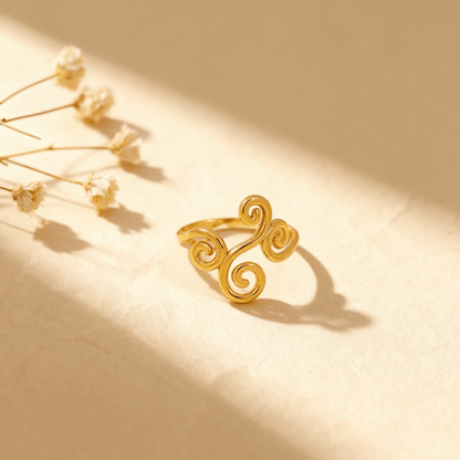 The Aphrodite Ring lying on a draped piece of shimmering, ivory silk fabric. The soft, luxurious texture of the silk enhances the ring's intricate, polished gold vine design and its romantic, ethereal quality.