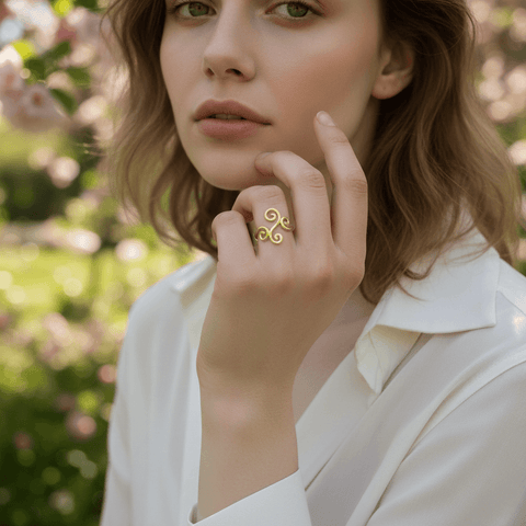 A soft-focus, romantic shot of a model's hand gently running through her wavy, sun-kissed hair, with the gold Aphrodite Ring visible on her finger. The image evokes a dreamy, carefree, and effortlessly feminine mood.