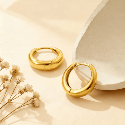A detailed close-up of a pair of the medium-sized gold Capsule Hoops, showcasing their smooth, rounded surface, high-polish finish, and seamless design on a neutral background.