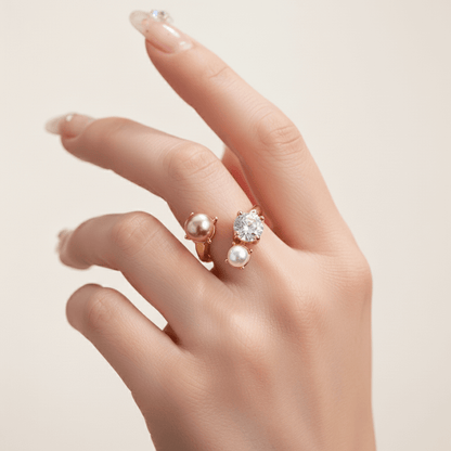 A close-up of a model's hand with a fresh, nude manicure, wearing The Celestial Ring in gold on her ring finger. The ring's open cuff design and the cluster of the crystal and pearls are beautifully showcased.