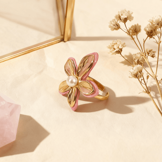 A top-down, perfectly centered shot of The Orchid Ring, showcasing the symmetrical arrangement of its four main gold petals and the central pearl. This view emphasizes its balanced, floral geometry and the pop of pink enamel on the edges.