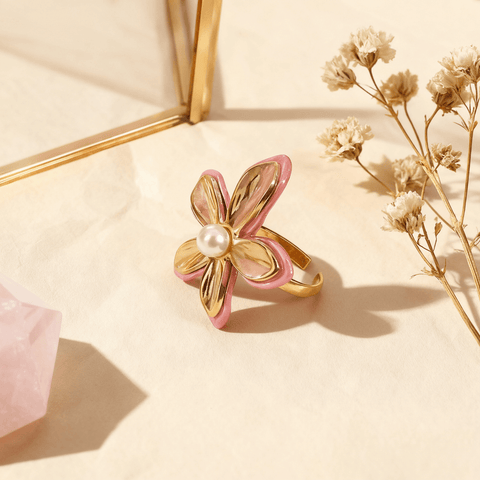 A top-down, perfectly centered shot of The Orchid Ring, showcasing the symmetrical arrangement of its four main gold petals and the central pearl. This view emphasizes its balanced, floral geometry and the pop of pink enamel on the edges.