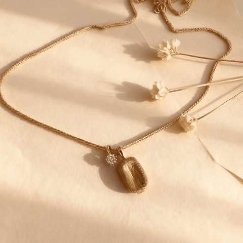The Signature Necklace, featuring a rectangular brushed gold tag pendant and a small, asymmetrical CZ crystal charm on a delicate gold chain, displayed on a clean white background.