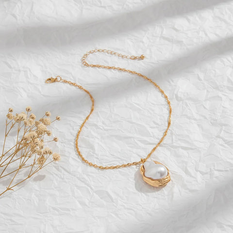 An artistic flat lay of The Theia Necklace, showing the full length of the adjustable gold rope chain and the organic shape of the pearl pendant.