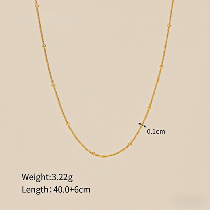 Extreme close-up of the dotted bead texture on the minimalist gold chain.
