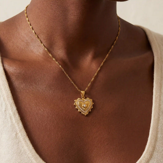 Close up of woman with dark skin wearing vintage gold heart medallion necklace with crystal center.