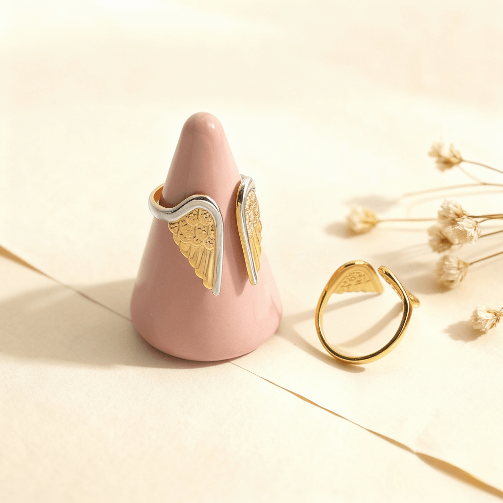 The two-tone Seraphina angel wing ring displayed on a creative pink ring cone, with the all-gold version resting beside it to showcase both styles.