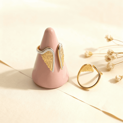 The two-tone Seraphina angel wing ring displayed on a creative pink ring cone, with the all-gold version resting beside it to showcase both styles.