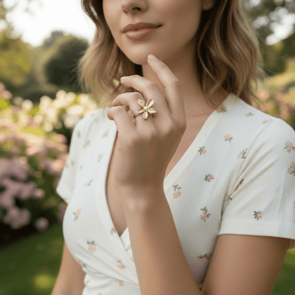 A close-up of a model's hand, adorned with the sculptural Orchid Ring, holding a fine-tipped paintbrush dipped in pink paint. This image frames the ring as a piece of wearable art, perfect for a creative spirit