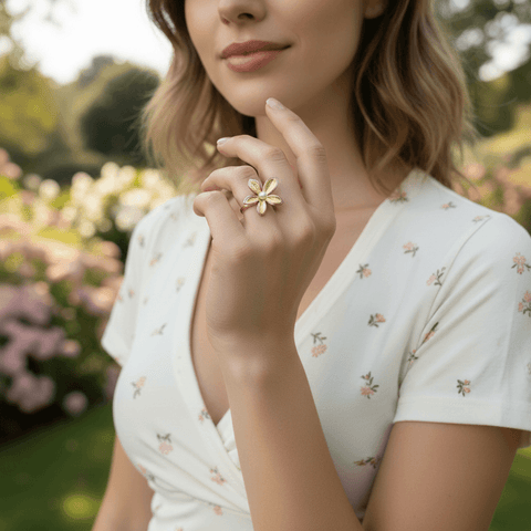 A close-up of a model's hand, adorned with the sculptural Orchid Ring, holding a fine-tipped paintbrush dipped in pink paint. This image frames the ring as a piece of wearable art, perfect for a creative spirit
