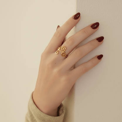 A beautiful shot of a model's hand held up towards the sun, with rays of light streaming through her fingers and highlighting the open, airy design of the gold Aphrodite Ring. It emphasizes the ring's lightweight and ethereal quality.