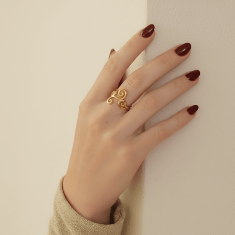 A beautiful shot of a model's hand held up towards the sun, with rays of light streaming through her fingers and highlighting the open, airy design of the gold Aphrodite Ring. It emphasizes the ring's lightweight and ethereal quality.