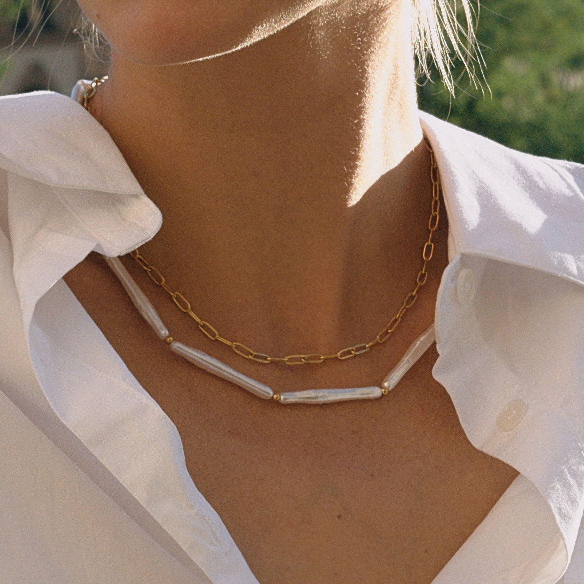 The Callisto Necklace worn by a model in bright sunlight, emphasizing the beautiful contrast between the lustrous stick pearls and the shining gold chain.