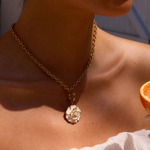 A stunning model with a deeper skin tone wearing The Fleur Pendant, showing the beautiful contrast of the white camellia and warm gold.