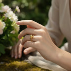 A woman wearing the all-gold Fluid Pebble Ring in a lush, green environment, showing it as a warm, sculptural piece of wearable art.