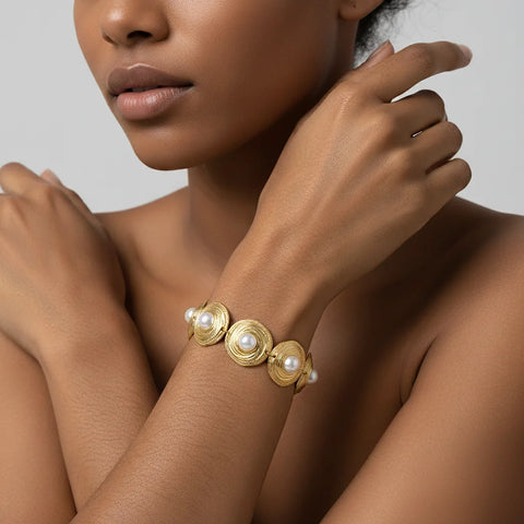 The Hera Bracelet worn by a model with a deeper skin tone, highlighting the beautiful contrast of the polished gold and pearls against her skin.