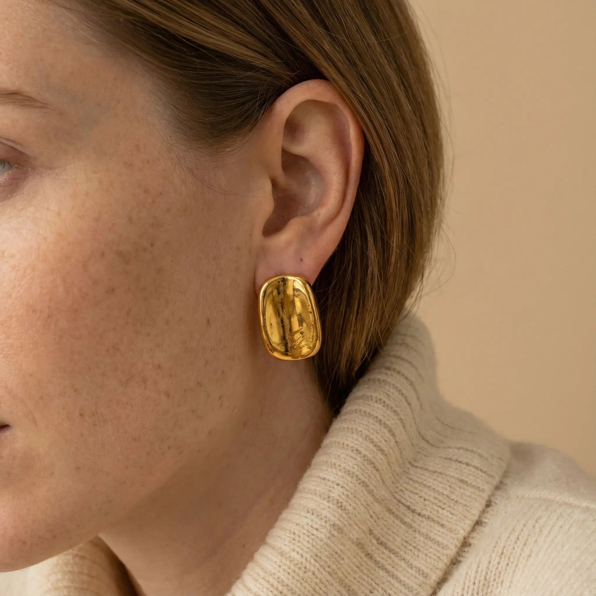 Close up of woman wearing Hestia chunky gold cushion shape stud earrings minimalist style. Main image