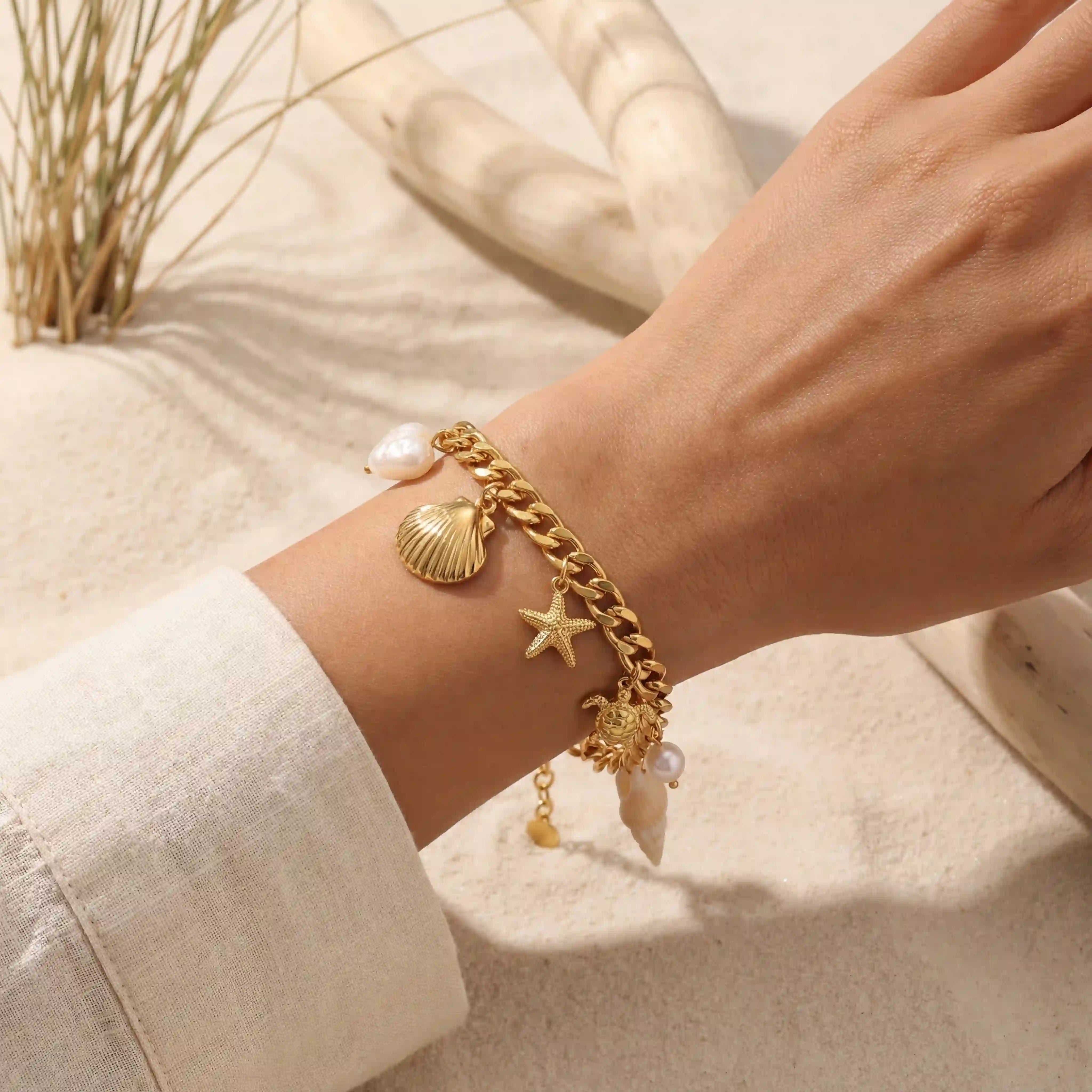 Close up of gold ocean charm bracelet with shell and starfish on woman wrist beach vibe.