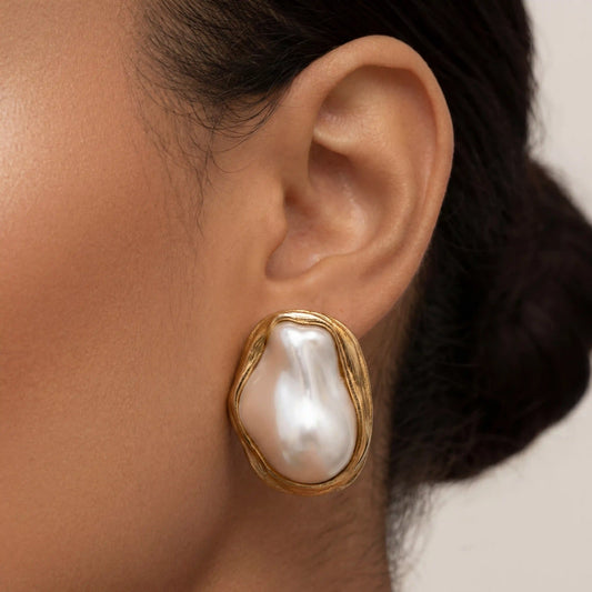 Side profile of a model with glowing skin wearing The Theia Earrings, highlighting their bold scale and how the organic gold setting curves around the earlobe.