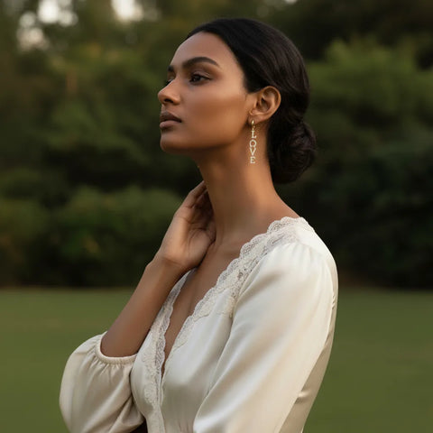 A model stands in a beautiful garden, her hair swept back to fully display the elegant drop and modern message of The Amor Earrings.