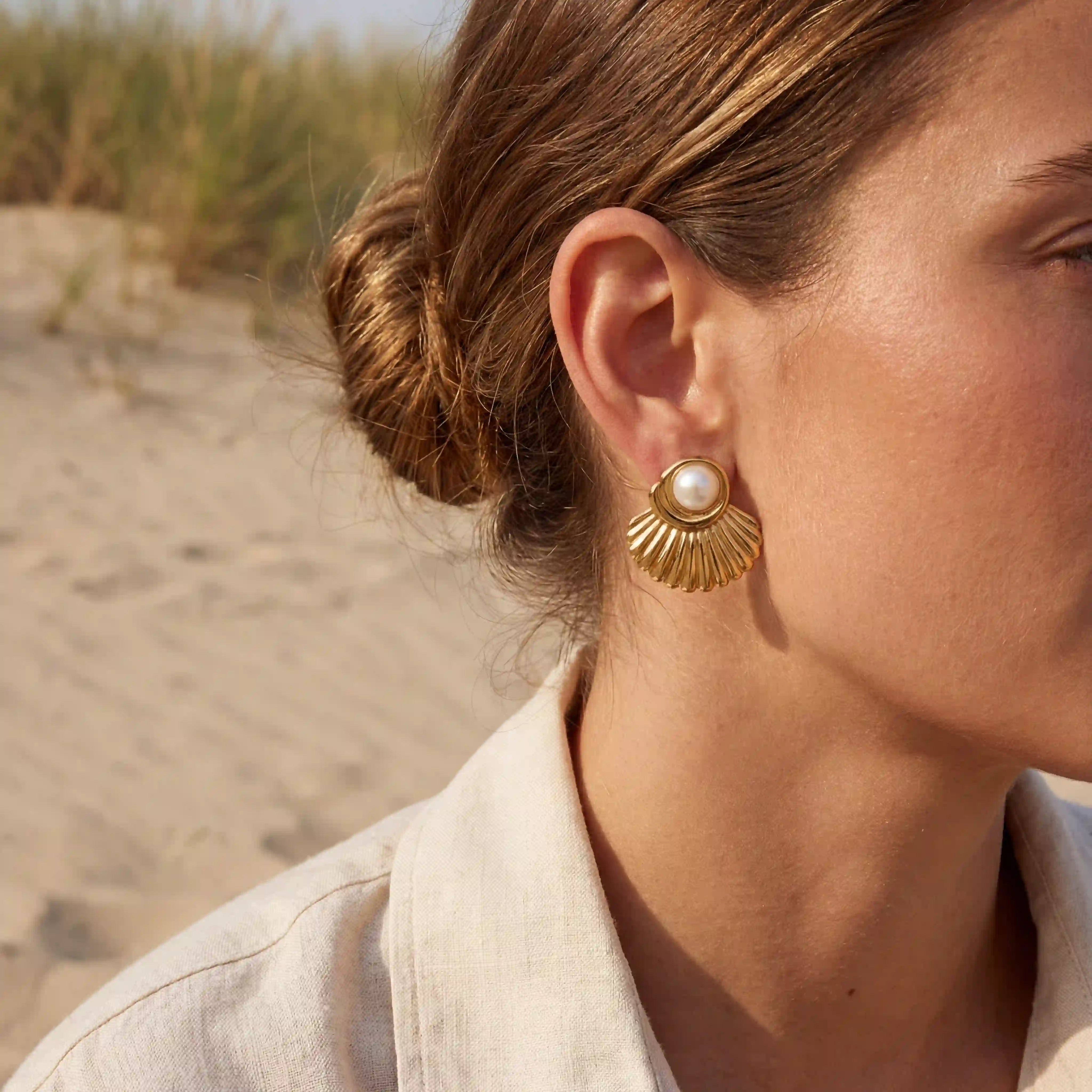 Side profile of woman wearing gold statement shell earrings at the beach.