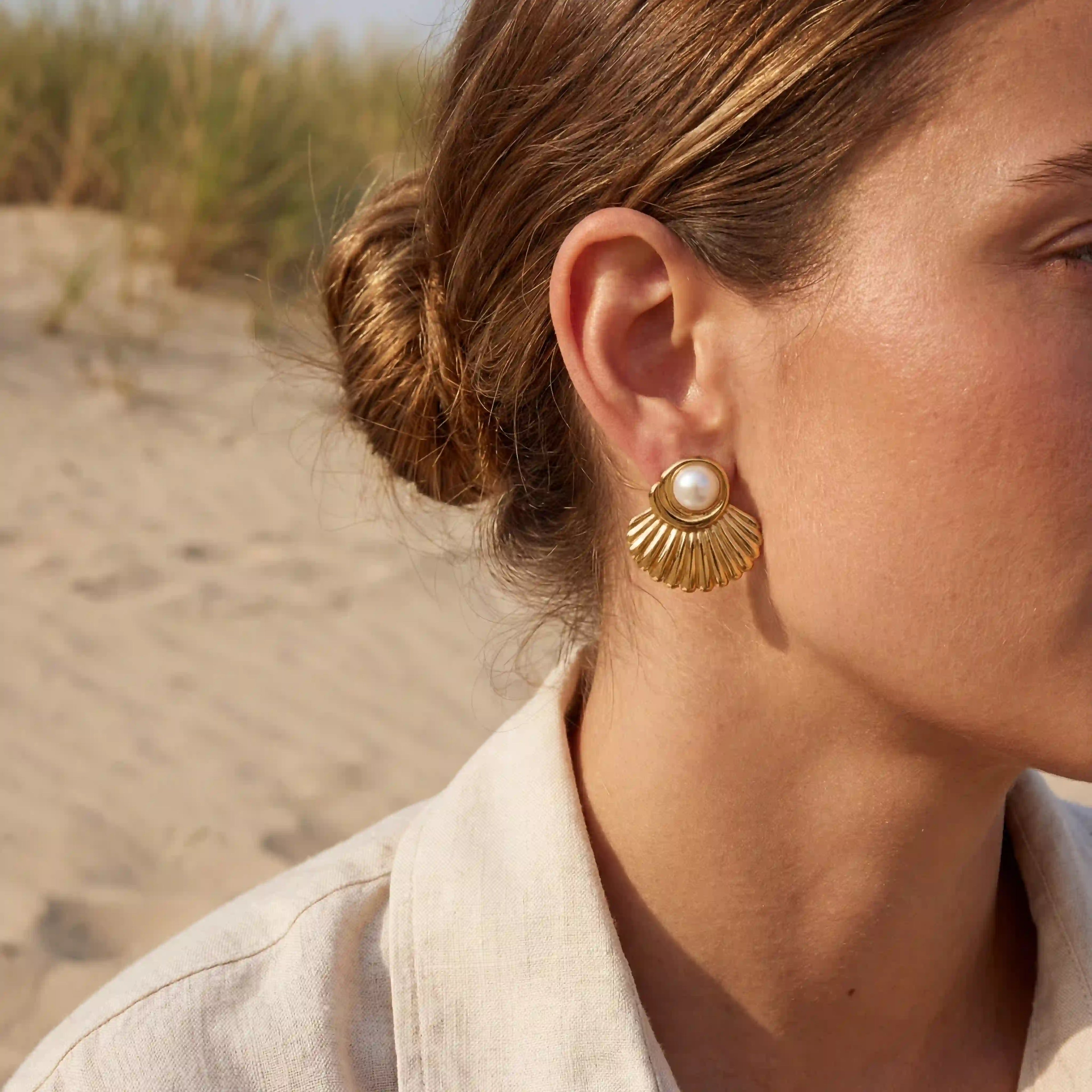 Side profile of woman wearing gold statement shell earrings at the beach.