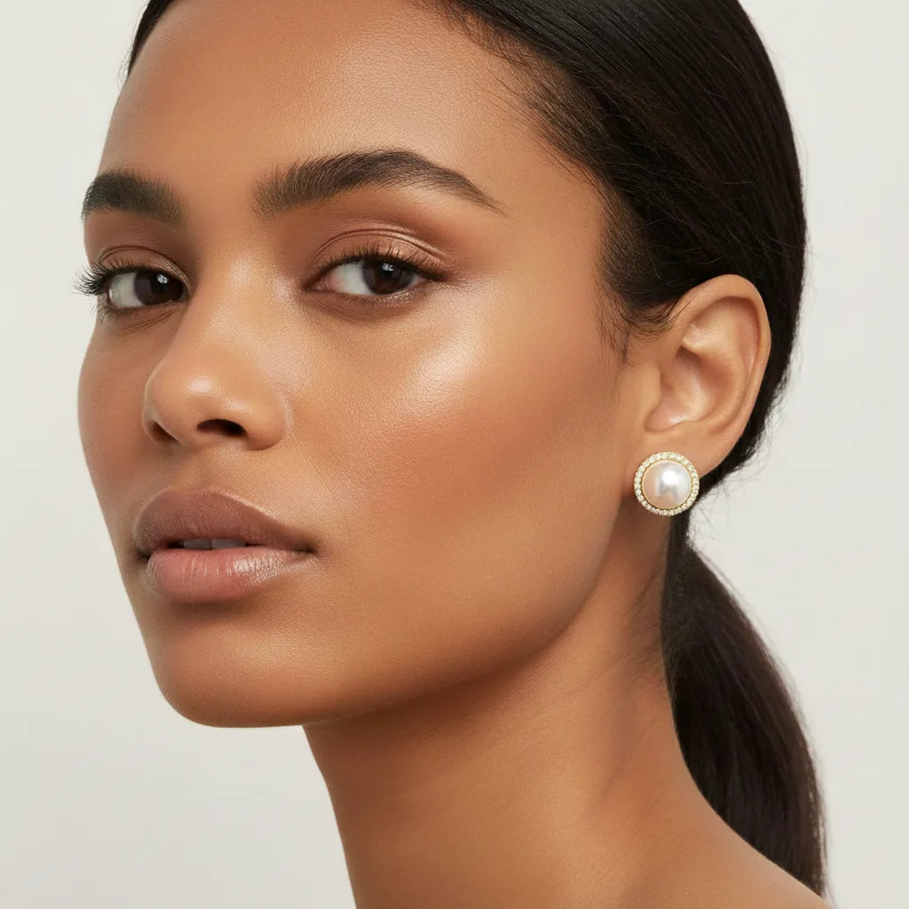 A beautiful model with a deeper skin tone wearing The Athena Studs, showing the stunning and versatile appeal of the classic pearl design on all complexions.