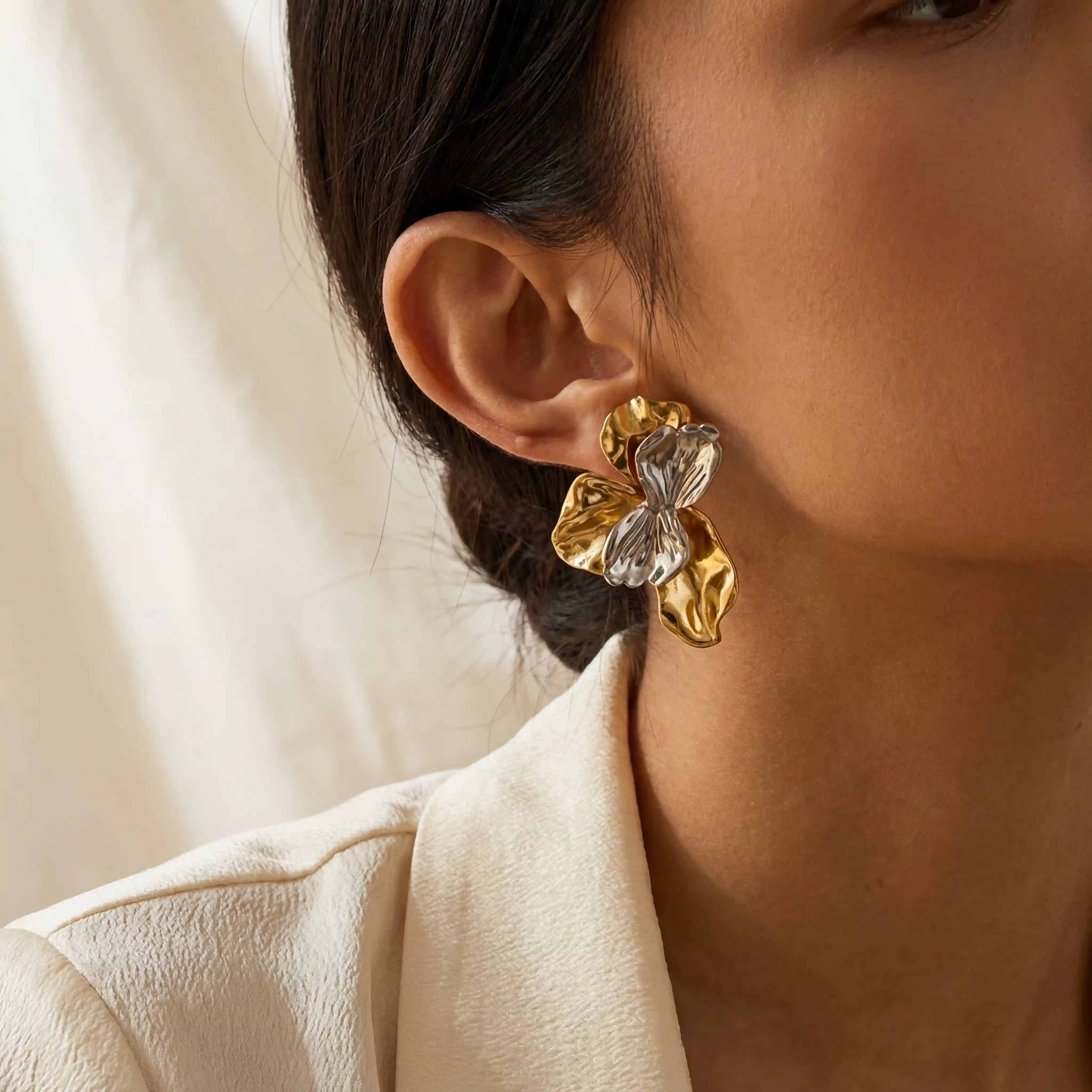 Close up of dark skin model wearing Aurora abstract earrings with molten gold and clear stone design. Main image