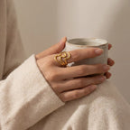 Woman holding coffee cup wearing gold wavy cadence ring cozy lifestyle.