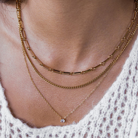 A beautiful close-up of a model wearing The Charites Necklace with a cozy white sweater, highlighting the perfect, effortless layering of the three distinct chains.