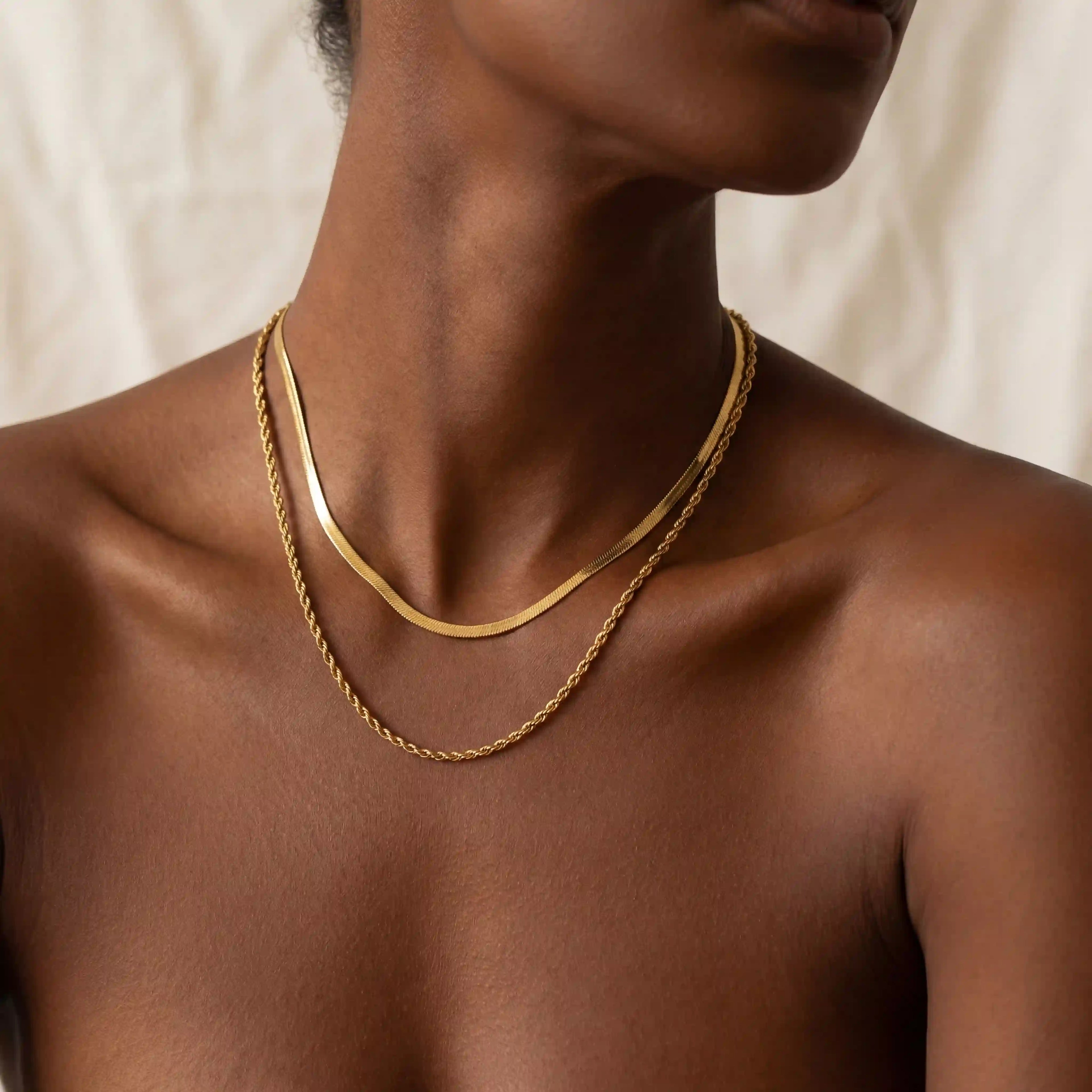 Close up of woman with dark skin wearing classic gold layered necklace with herringbone and rope chains.
