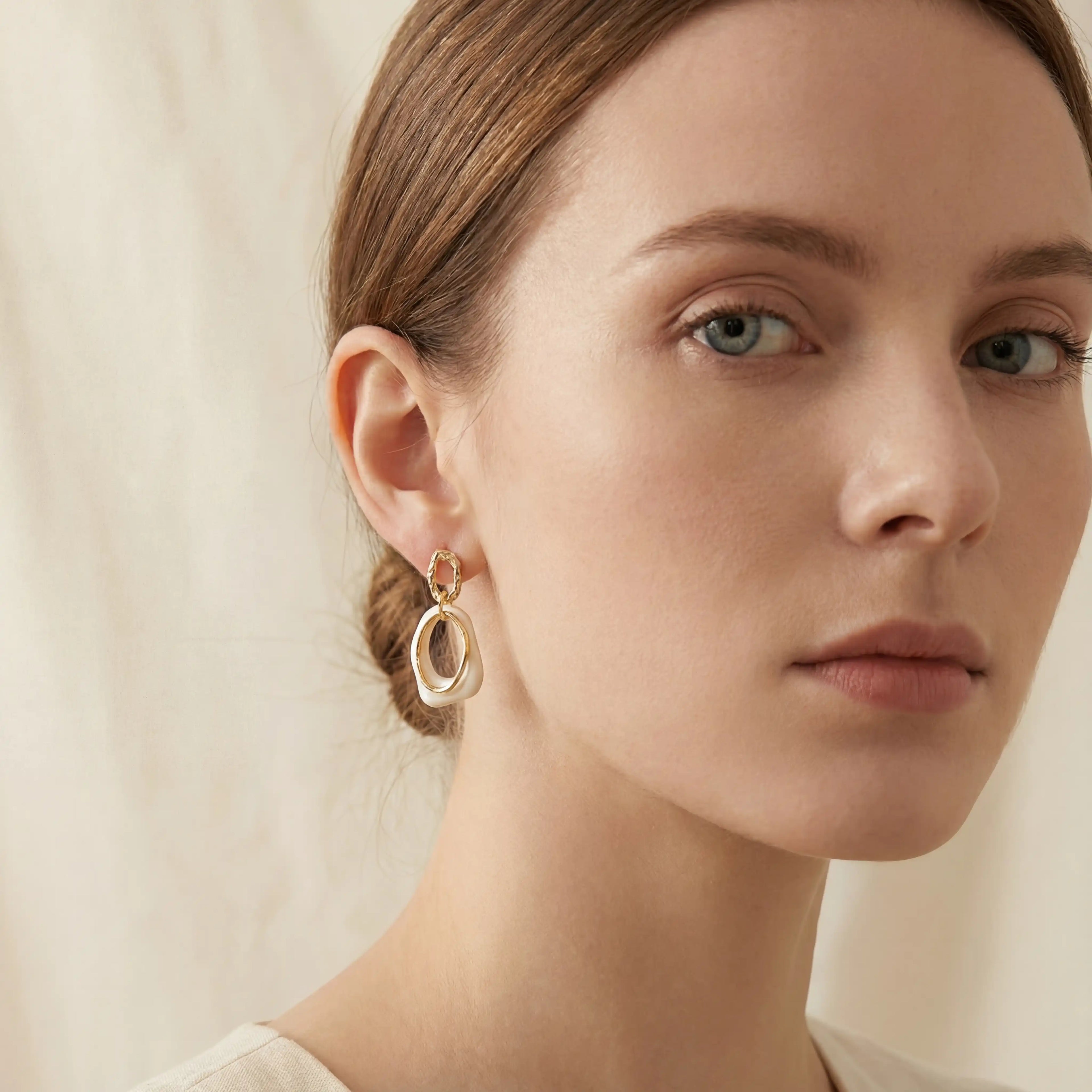 Elegant model styling ivory enamel gold earrings for work or date.