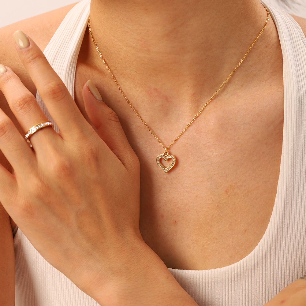 A model wearing The Devotion Necklace, her hands with a ring visible, illustrating how the delicate heart pendant can be styled with other jewelry.