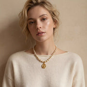 Blonde woman styling chunky pearl necklace with cream sweater winter chic look.