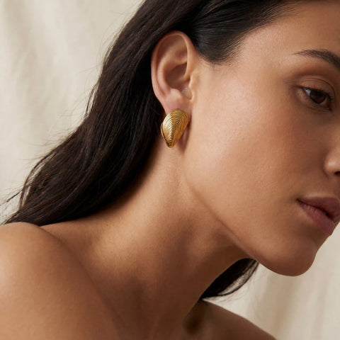 Side profile of woman wearing gold statement shell earrings ocean inspired style.