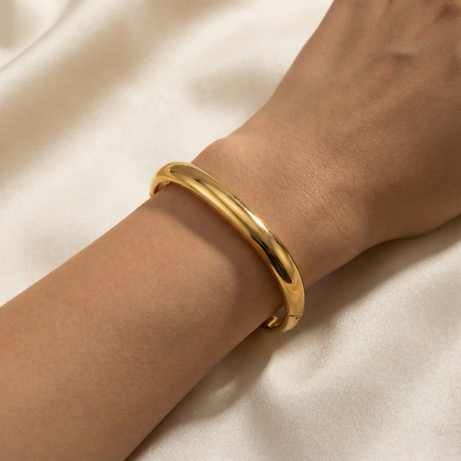 Woman wearing single gold square bangle on silk background minimalist jewelry.