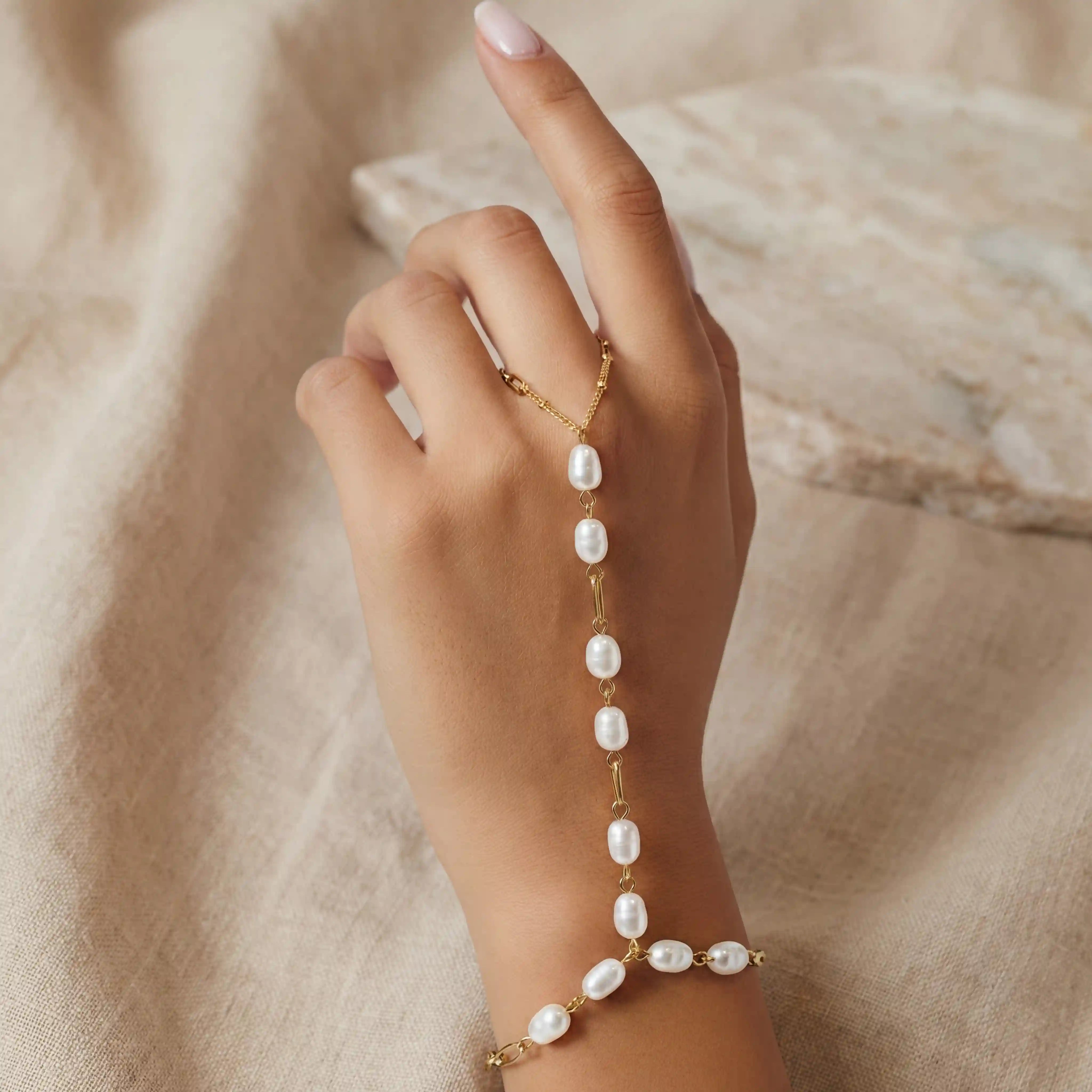 A model's hand with her finger raised, showing the delicate fit of the pearl finger loop on The Nereid Hand Chain. Main image