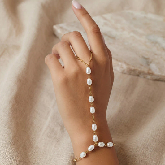 A model's hand with her finger raised, showing the delicate fit of the pearl finger loop on The Nereid Hand Chain.