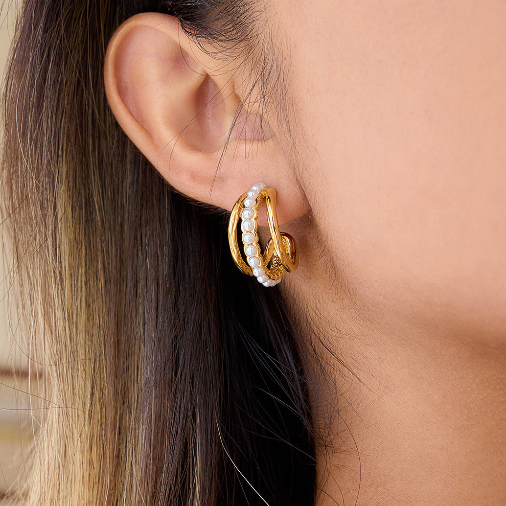 A close-up of a model wearing The Siren Hoops, highlighting their bold, chunky size and how the layered pearl and gold design elegantly hugs the earlobe.