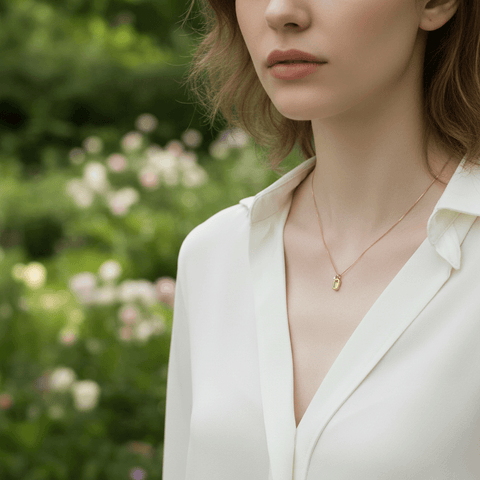 A close-up of a model's hand gently holding the brushed gold tag of her Signature Necklace. This intimate gesture suggests a personal connection to the piece, highlighting its role as a meaningful, signature accessory.
